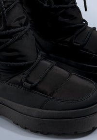 Czarne botki za kostkę z miękką, nylonową cholewką, teksturowaną gumową podeszwą i grubymi sznurowadłami. Charakteryzują się solidną konstrukcją z platformową podstawą.