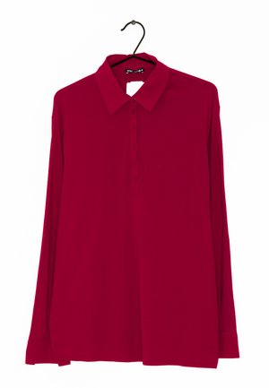 Polo à manches longues de couleur rouge uni, avec un col pointu, une patte de boutonnage et une texture de tissu lisse. Suspendu à un crochet noir.