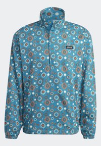 Blå tröja med halv dragkedja, prydd med ett mönster av solmotiv i orange, vitt och blått. Tillverkad av strukturerad tyg med elastiska ärmslut.