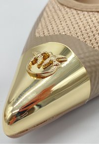 Scarpa beige a punta con tomaia strutturata, punta dorata con un motivo decorativo a foglia e finitura liscia e lucida.