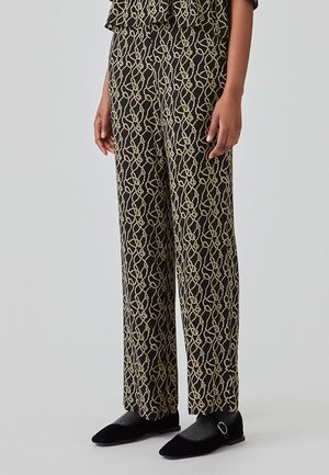 Pantalons noirs avec un motif abstrait doré, coupe large, texture lisse, accompagnés de ballerines noires et de chaussettes grises, visibles au niveau de la cheville.