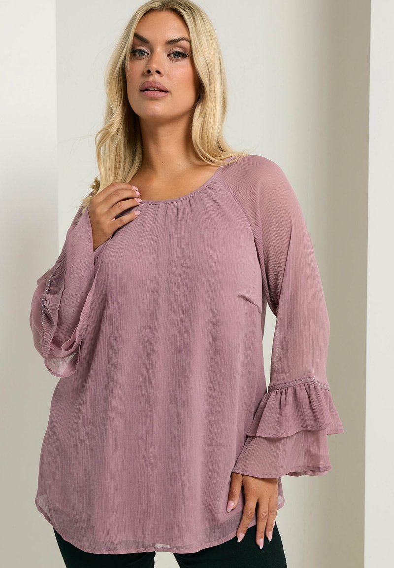 Blusa mauve ampia con maniche lunghe e volant. Presenta un colletto rotondo e un tessuto texturizzato con pieghe sottili. Leggera e fluida.