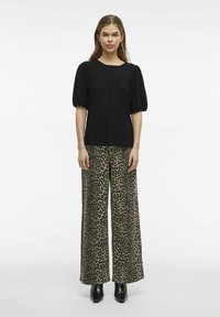 Svart, texturerad kortärmad topp i kombination med vida leopardmönstrade byxor. Modellen bär svarta klackstövlar. Enkelt, modernt snitt.