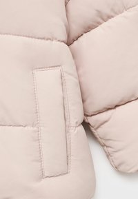 Ljusrosa puffjacka med kviltad textur, ett sömnadsområde och en liten lapplomme på ärmen. Mjukt och smidigt material.