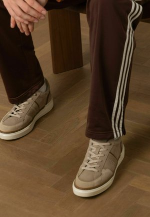 Lichtbruine sneakers met suède en leren accenten, witte rubberen zool, vetersluiting. Gemaakt met donkere broek met witte zijstrips.