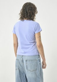 Fliederfarbenes Kurzarm-T-Shirt aus weichem Baumwollstoff, taillierte Passform und abgerundeter Saum. Kombiniert mit hoch geschnittenen hellblauen Jeans.