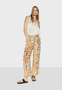 Färgglada mönstrade vida byxor med livfulla färger, geometriska mönster och ett matchande bälte, i kombination med en vit ärmlös topp och svarta sandaler.