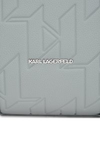 Sac en cuir gris avec des motifs géométriques en relief, affichant un logo "KARL LAGERFELD" en argent positionné de manière proéminente en bas.