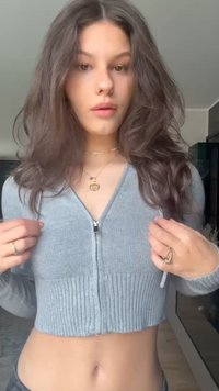 Sweater cinza cropped com fecho éclair, de textura canelada e mangas longas, apresentando um fecho prateado e um design minimalista.