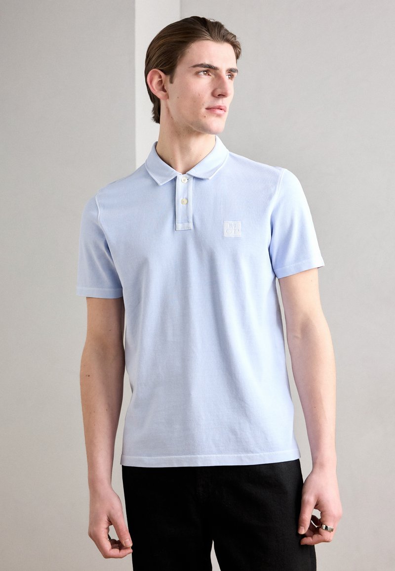 Polo di colore azzurro chiaro con colletto classico, maniche corte e tessuto testurizzato, dotato di un piccolo logo sul lato sinistro del petto.