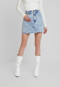 Minigonna in denim lavaggio chiaro con orlo sfrangiato, vita alta e tasche anteriori, abbinata a stivali bianchi al ginocchio.