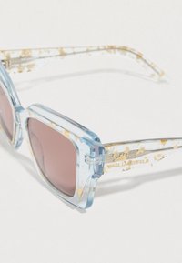 Διαφανή γαλάζια γυαλιά ηλίου με χοντρό τετράγωνο πλαίσιο, που διαθέτουν χρυσές πινελιές και ροζ φακούς με χρωματισμό. Διακοσμημένα με το λογότυπο της μάρκας στα πλαϊνά.