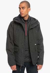 Schwarze isolierte Jacke mit durchgehendem Reißverschluss, verstellbarem Kapuze, mehreren Taschen und roten Akzenten. Hergestellt aus strapazierfähigem, wetterbeständigem Material.