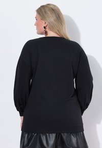 Suéter negro de manga larga con un corte relajado y mangas abullonadas, combinado con una falda de cuero negro. Textura suave, cuello redondo básico.