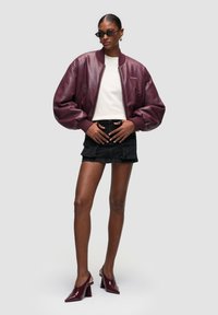 Bomber bunda z bordové kůže s nafouklými rukávy, doplněná bílou košilí a černou džínovou sukní, a bordó lodičky na podpatku.