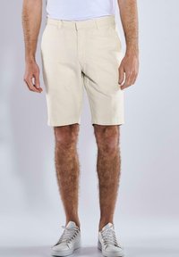Beige, knee-length shorts made from a textured fabric, featuring belt loops and side pockets, paired with white sneakers.
