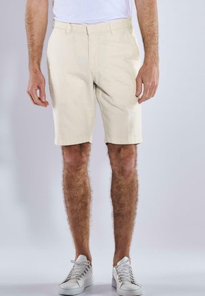 Beige, knee-length shorts made from a textured fabric, featuring belt loops and side pockets, paired with white sneakers.