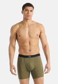 Miesten oliivinvihreät bokserialushousut, joissa musta vyötärönauha ja logo. Sileä kangas, istuva malli ja reisien puoliväliin ulottuva pituus.