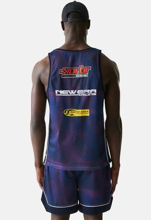 Mann trägt ein marineblaues Renn-Trikot aus Mesh und passende Shorts mit Logos auf der Rückseite, dazu eine schwarze Baseballkappe, schaut nach hinten.