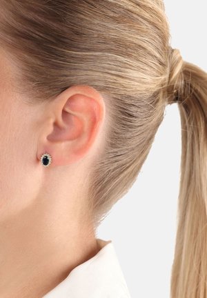 Orecchini rotondi con un grande gemma nera centrale circondato da un alone di piccole gemme trasparenti, montati in metallo di tonalità argento.