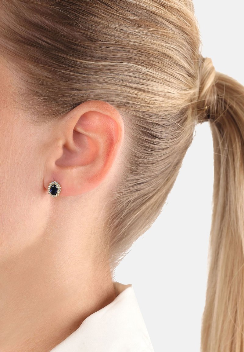 Runda örhängen med en centralt svart ädelsten omgiven av en halo av små klara stenar, i en silverfärgad metall.