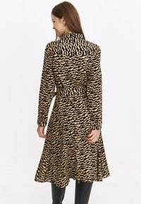 Langärmliges Kleid in einem welligen Schwarz- und Beige-Muster; verfügt über einen Kragen, einen Gürtel in der Taille und einen ausgestellten Rock.