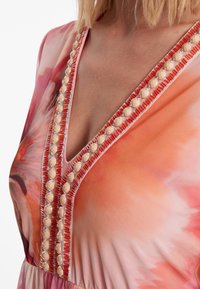 Blumengemusterte Kleid in Pink- und Orangetönen, mit einem V-Ausschnitt, der mit cremefarbenen Perlen und kontrastierendem roten Saum verziert ist.