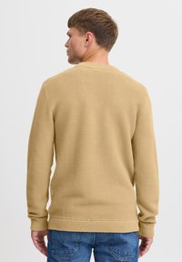 Langärmliger, gerippter Pullover in hellbraun. Merkmale: Rundhalsausschnitt und weiche Textur, kombiniert mit blauen Jeans. Rückansicht gezeigt.