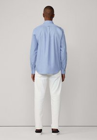 Lichtblauw overhemd met lange mouwen, witte broek en donkere schoenen. Het overhemd heeft een eenvoudig ontwerp en een plooidetail op de rug.