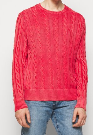 Pull en tricot rose à motif torsadé avec des poignets et un ourlet côtelés. Associé à un jean bleu, mettant en valeur une silhouette ajustée.