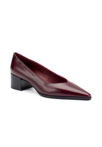 Zapato de tacón en burdeos con punta afilada y tacón bajo. Presenta una textura suave y un diseño limpio y minimalista.