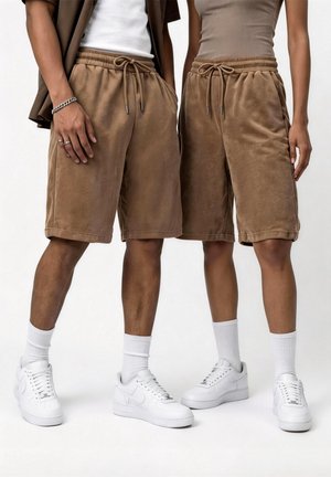 Deux personnes portant un short marron assorti avec cordon, des chaussettes blanches et des baskets blanches, debout côte à côte devant un fond uni.