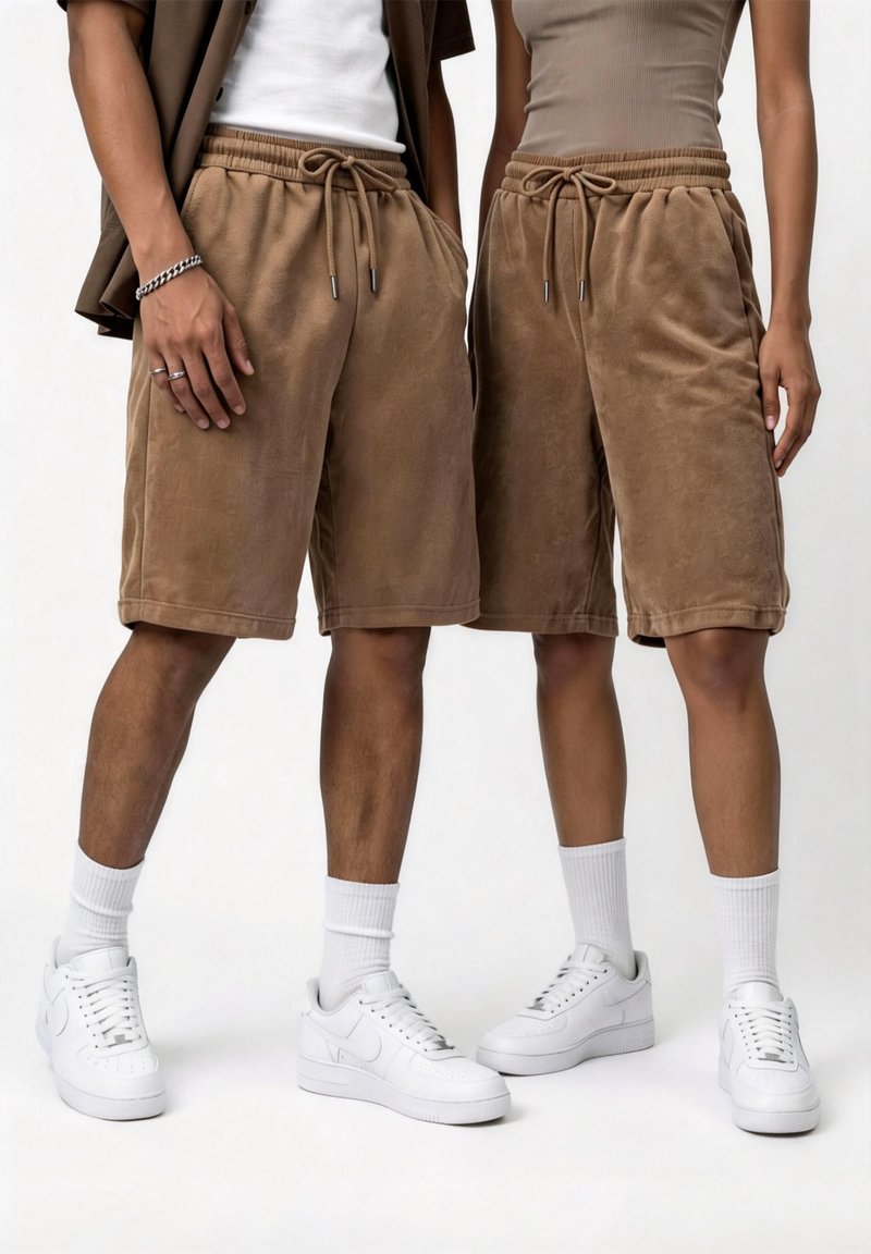 Δύο άτομα φορούν ίδια καφέ σορτσάκια με κορδόνι, λευκές κάλτσες και λευκά αθλητικά, στέκονται δίπλα-δίπλα σε απλό φόντο.