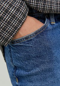 Pantalones vaqueros de denim azul con textura deslavada y costuras amarillas, combinados con una camisa de patrón en blanco y negro con un diseño tejido.