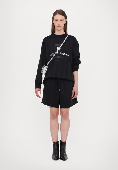 Black oversized sweatshirt with white text, paired with black shorts. Model wears knee-high black boots with silver accents and a silver crossbody bag.