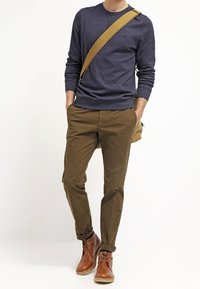 Námořnický svetr, khaki chinos a hnědé kožené kotníkové boty. Obsahuje světlou messenger tašku s popruhem. Jednoduchý, neformální outfit.