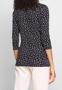 Námořnický top s tříčtvrtečními rukávy, který obsahuje bílý kruhový vzor. Měkká tkanina, slim fit, zakulacený spodní lem, nošený s krémovými kalhotami.