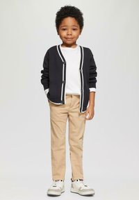 Marineblauwe cardigan met witte biezen en knopen, witte t-shirt, beige broek en witte sneakers met grijze accenten, geschikt voor kinderen.