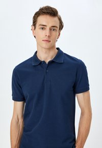 Mörkblå polo-tröja i bomull, med en stickad krage, korta ärmar med ribbade manschetter och en tre-knappars knäppning.