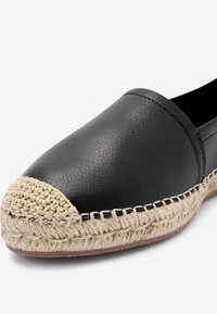 Schwarze Leder-Espadrille mit abgerundetem Zehenbereich, gewebtem Jutebesatz und beigen Häkel-Details vorne. Insgesamt glatte Textur.