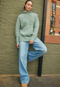 Miętowe, oversize'owe hoodie z haftem "1999" z przodu, w połączeniu z luźnymi, jasnoniebieskimi dżinsami o swobodnym kroju i ściągaczami na rękawach.