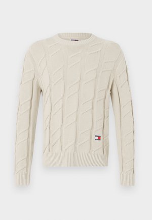 Kremowy sweter z dzianiny z wzorem w warkocze, okrągłym dekoltem oraz ściągaczami przy mankietach i dolnej krawędzi. Mała łatka z logo na dolnej lewej stronie.