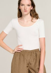 White short-sleeve bodysuit with a scoop neck, paired with loose brown pants, featuring a textured fabric and elastic waistband.