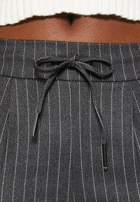 Pantalons gris à rayures avec une taille à cordon de serrage noué, ornés d'accents en métal argenté aux extrémités du cordon.