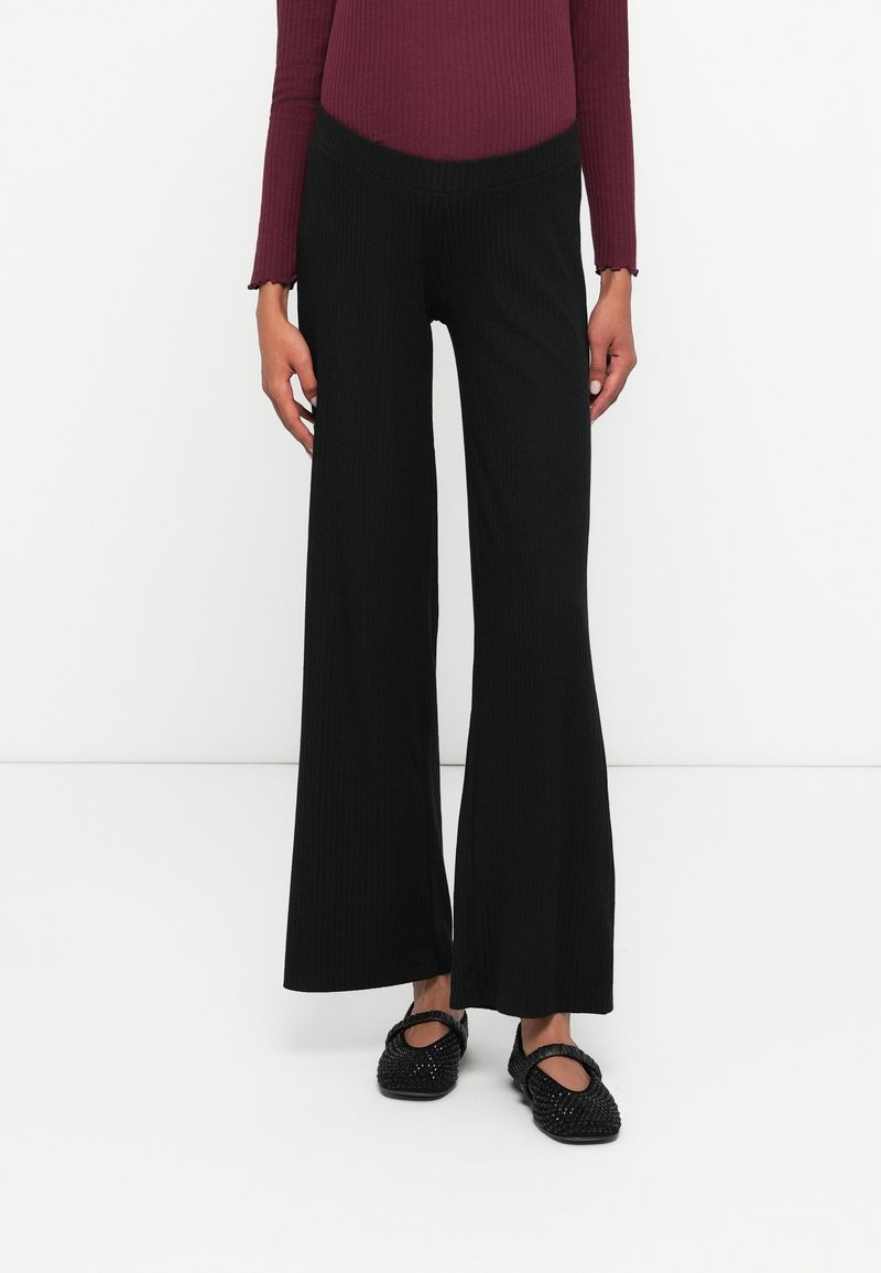 Svart randig byxa med vida ben och hög midja, med en texturerad design. Matchas med svarta prydnadsballerinas för kontrast.