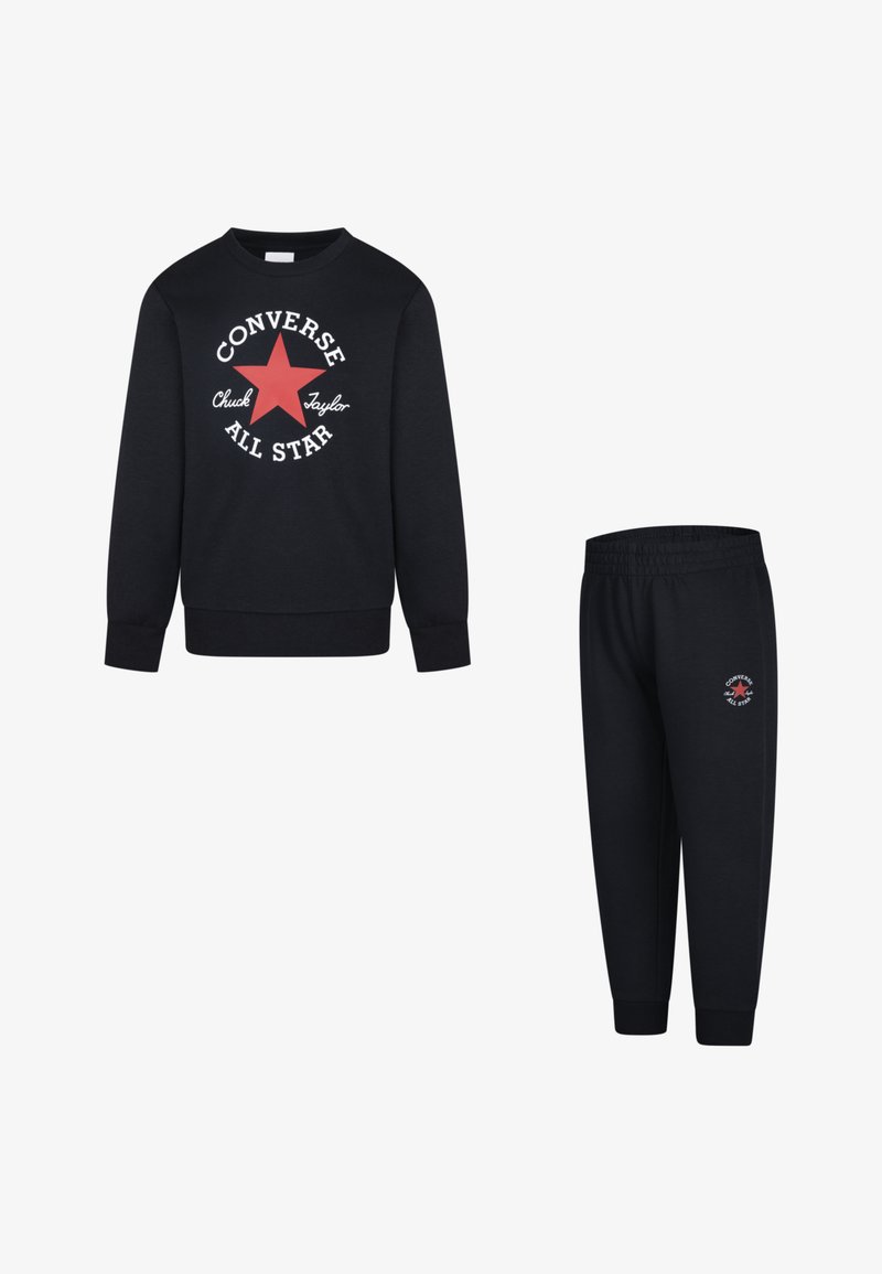 Črn komplet s sweatshirtom in trenirkami, ki vključuje rdečo zvezdo in belo besedilo. Mehka tkanina, rebrasti manšeti in elastičen pas na trenirkah.