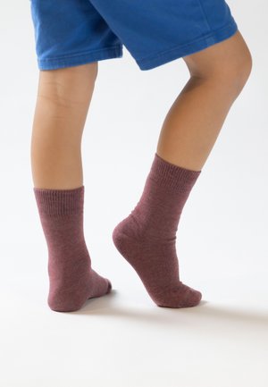 Bordeauxfarbene Baumwollsocken mit gerippten Bündchen, getragen an den Füßen, kombiniert mit blauen Shorts. Die Textur wirkt weich und dehnbar, ideal für Freizeitbekleidung.