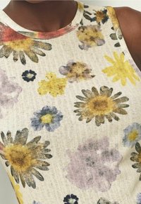 Débardeur à fleurs en tissu beige texturé avec un mélange de fleurs jaunes, violettes et noires dans un style aquarelle. Encolure ronde.
