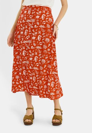 Falda midi roja con estampado tropical blanco, combinada con top blanco y sandalias de plataforma marrones con tiras en el tobillo.