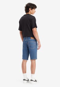 Tricou scurt negru, pantaloni scurți din denim albastru cu cinci buzunare, etichetă din piele pe spate, șosete albe și adidași negri cu dungi laterale.